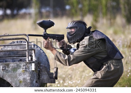 Protective sport player in uniform and mask Aiming gun, behind a jeep