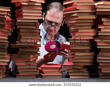 Man surrounded with books,examining a CD that has in the hand