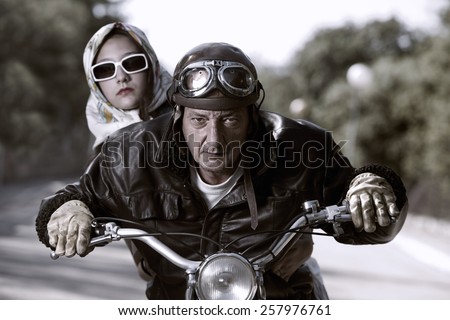Old biker with helmet and goggles, accompanied by a woman with glasses and headscarf