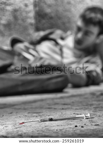 Young drug addict lying on the ground, with a syringe in the first plane