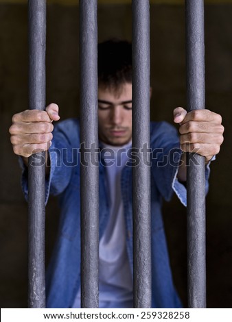 Imprisoned man, looking down, seized to a few bars