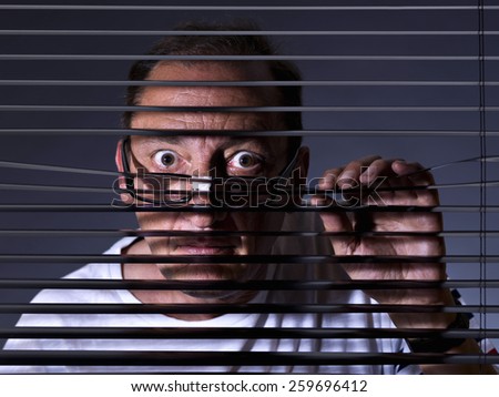 Vicious man looking sideways through venetian blind