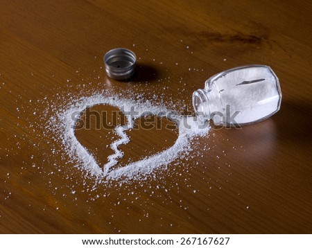 Salt shaker dump on a table and spilled salt forms a broken heart