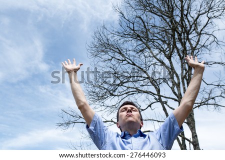 Man with open arms to the sky in front of a leafless tree