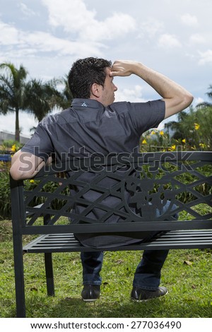 Man sitting in the chair back looking at the scenery in the park with his hand on his forehead