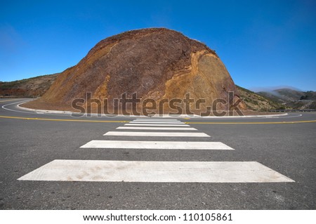 A sharp curve in a road in the mountains around a hill.