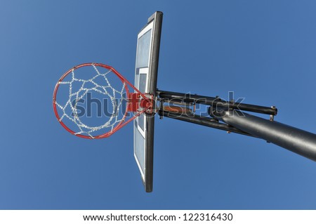 Blue sky behind a basketball backboard, hoop and chain net with pole