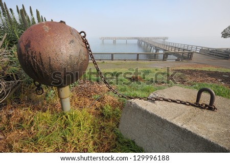 A large metal ball with chain is attached to a concrete block near a pier