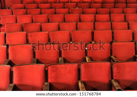 Old theater with rows of red seats with wooden arm rests