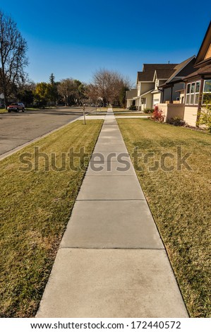 Long sidewalk next to street with grass and houses on the side