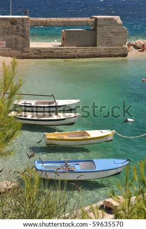 Four open boats at anchor by a beach.