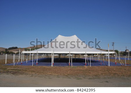 A white tent covers an empty space with hills in the background