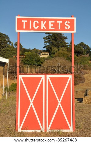 An empty ticket booth in a field with hay stacks.