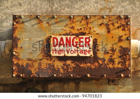 A wall with a rusty box with a Danger high voltage sign on it