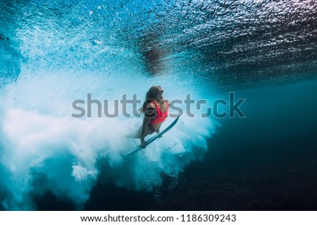 Surfer woman with surfboard dive underwater with under ocean wave.