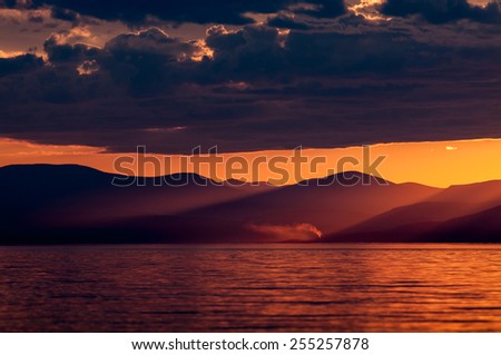 Smoking chimney on the opposite shore of the Baikal lake, with the mountains behind