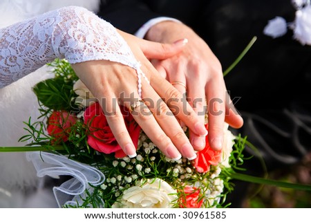 hands of a newly-married couple on a background of a bouquet