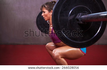 Fit attractive female athlete in sexy outfit performs barbell squat in gym.