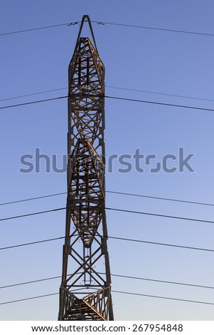 High tension electrical tower side faced, background smooth blue sky.