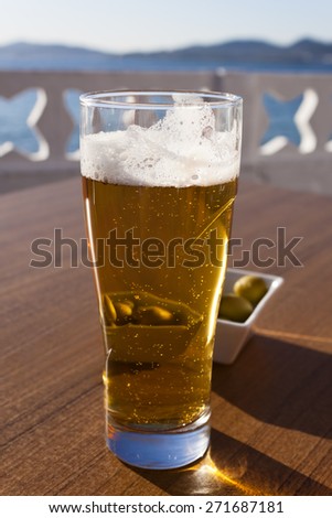 A glass of beer and a plate of olives behind in a table of a terrace next to the sea in Spain.