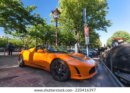 AMSTERDAM - NETHERLANDS: AUGUST 13, 2014: Orange electric Tesla car charging on the street plug.