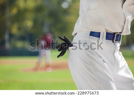 Closeup of black leather gloves in the back pocket of a baseball player in white jersey.