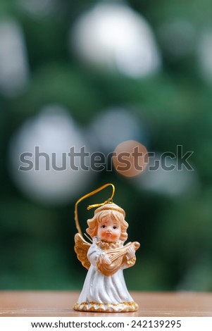 Small decorative angel ornament with Christmas tree in the background.