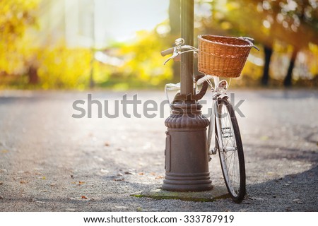 Vintage white bicycle with wooden basket locked to the street lamp in park. Post processed with sunny filter.