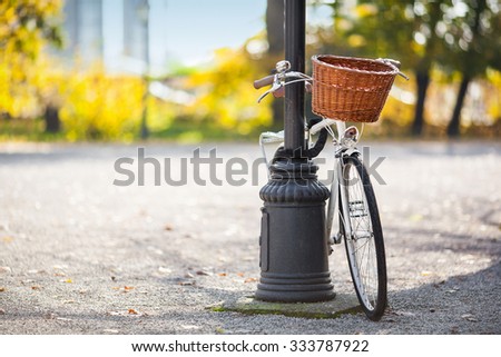 Vintage white bicycle with wooden basket locked to the street lamp in park.