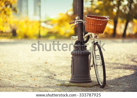 Vintage white bicycle with wooden basket locked to the street lamp in park. Post processed with vintage film filter.