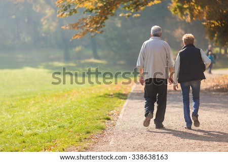 Senior citizen couple taking a walk in a park during autumn morning.