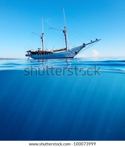 Sail boat in tropical calm sea on a surface and underwater sea view with sun beams