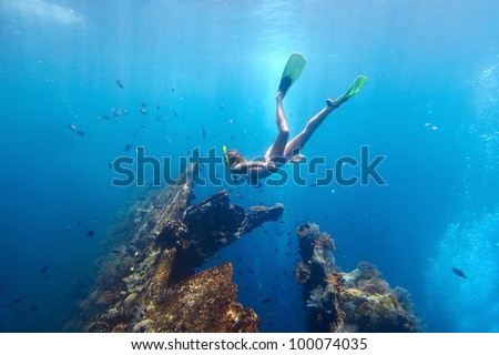 Young woman diving on a breath hold and fining in blue transparent sea near wreck USAT Liberty, Tulamben, Indonesia