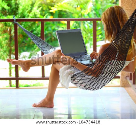Young woman sitting in a hammock in garden with laptop