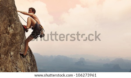 Young man climbing on a limestone wall with wide valley on the background