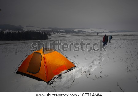 Two backpackers in a winter field and orange tent set on a snow