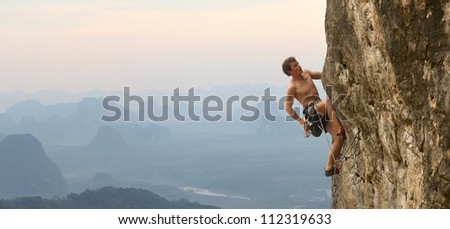 Young man climbing vertical wall with valley view on the background