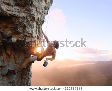 Young Man Climbing Vertical Wall With Belay With Sunrise Valley On The Background