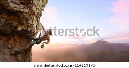 Young man climbing vertical wall with belay with sunrise valley on the background
