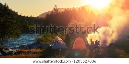 Panorama of the camp in the wild area. Hikers set the tents near the river and make fire at sunset