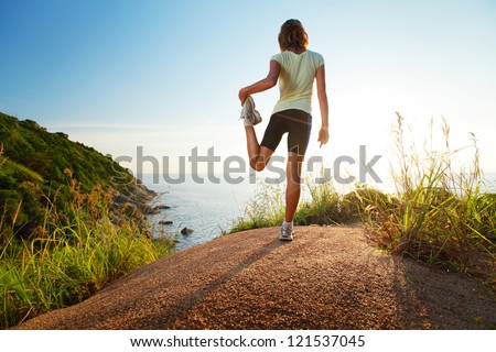 Cross Country Runner Stretching On Top Of A Hill And Enjoying Sunset Sea View