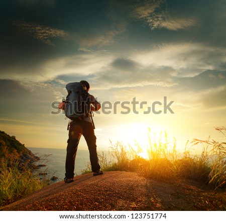 Hiker With Backpack Standing On A Rock And Enjoying Sunset Over Sea