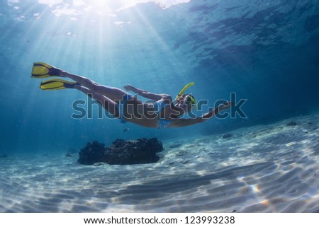 Underwater full length portrait of a woman snorkeling in tropical sea over sandy bottom