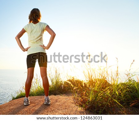 Young slim lady worn training clothes standing on countryside path and enjoying sunset