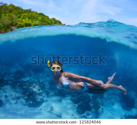 Underwater shoot of a young lady doing skin diving in tropical sea with green island on the background