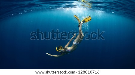 Underwater shoot of a young lady diving on a breath hold in a clear profound sea with sunbeams shining through the water