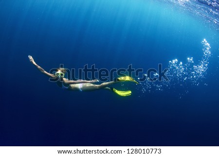 Underwater shoot of a young lady diving on a breath hold in a clear profound sea with sunbeams shining through the water