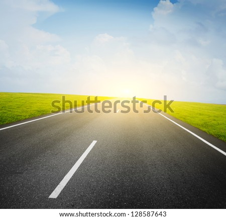 Asphalt road and green meadow and blue cloudy sky