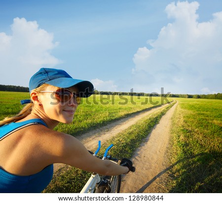 Young smiling lady cycling on a countryside road at summer sunny day