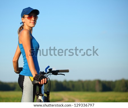 Slim lady standing with bicycle in a summer meadow at sunny day